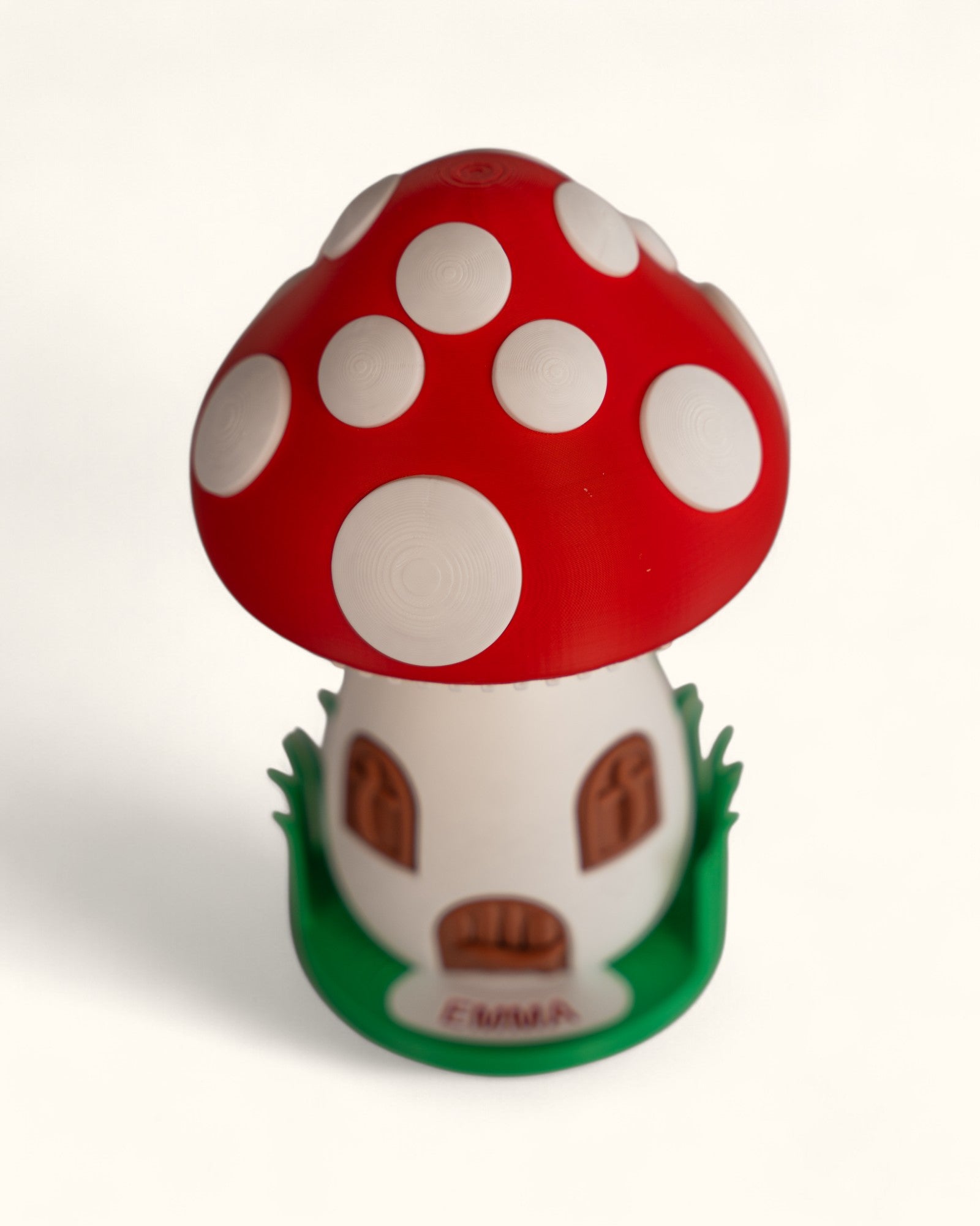 3D printed mushroom jewelry organizer with white spots, doors, windows as storage and green grass ring holder base and custom text printed on doorstep.