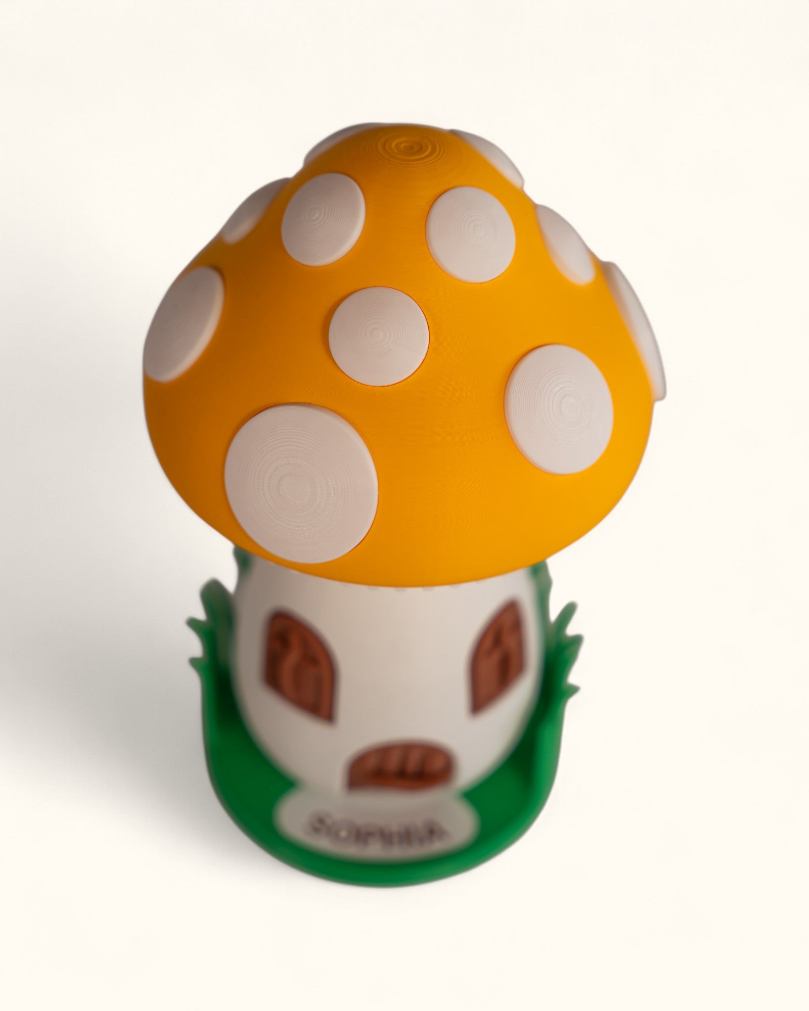 3D printed mushroom jewelry organizer with white spots, doors, windows as storage and green grass ring holder base and custom text printed on doorstep.